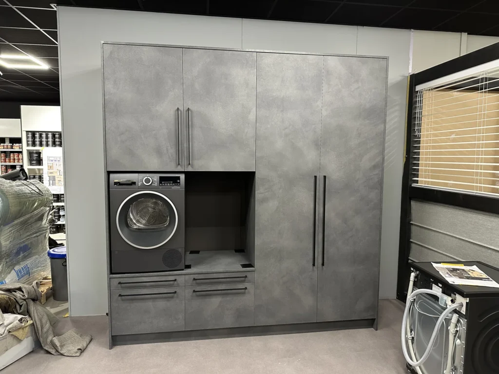 Wasmachinekast op maat in betonlook met een open nis en zwarte grepen