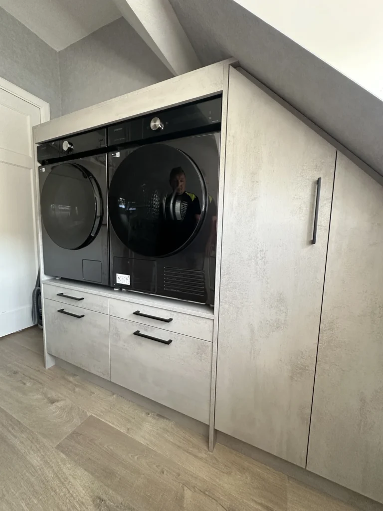 Witte wasmachinekast onder de dakschuinte met open apparatennis en hoge bergruimte
