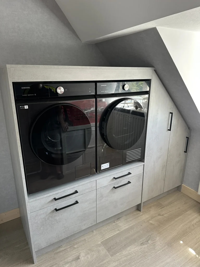 Frontaanzicht van een witte wasmachinekast op maat onder een schuin dak